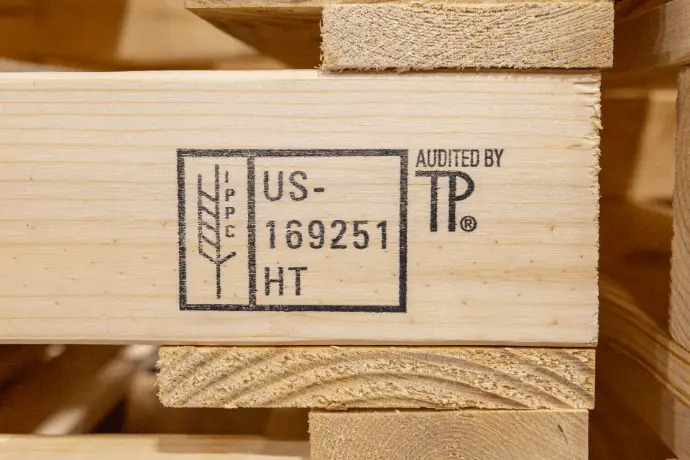 Close-up of an ISPM-15 heat treatment stamp on a wood shipping crate board, reading IPPC, US-169251, HT, audited by TP